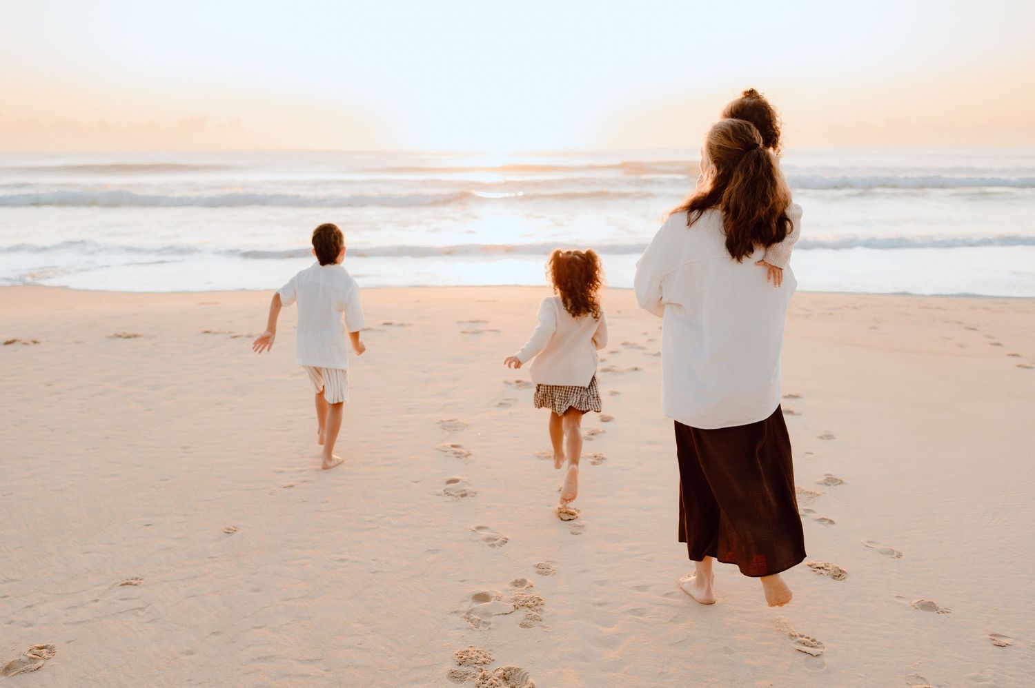 People walking along beach leaving footprints in sand during sunset.