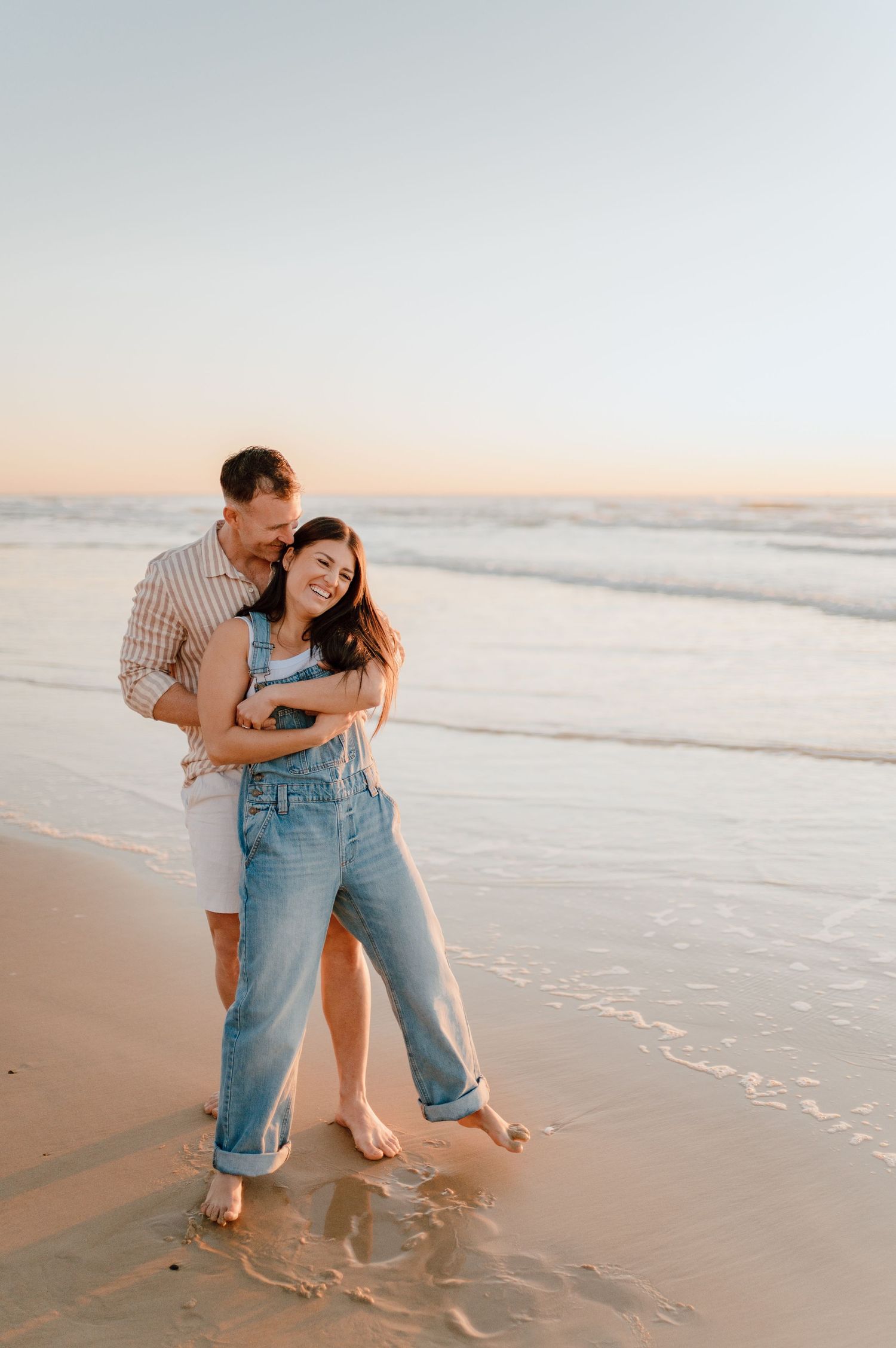 A couple embraces and dances together on a sandy beach at sunset.