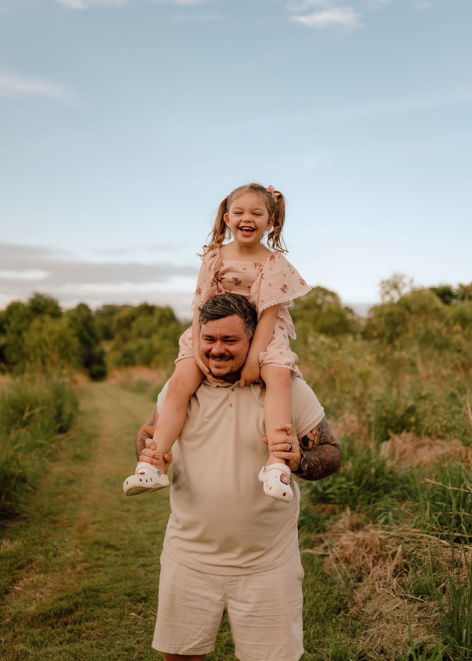A joyful moment captured outdoors as a child rides on shoulders while walking along a nature path in warm sunlight.