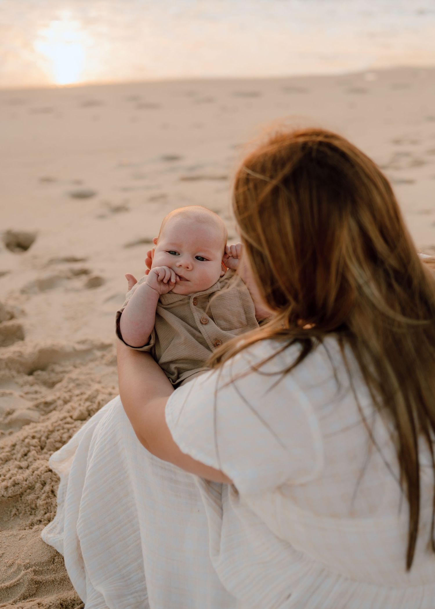 Sweet interactions between parent and baby on sandy beach at sunset.