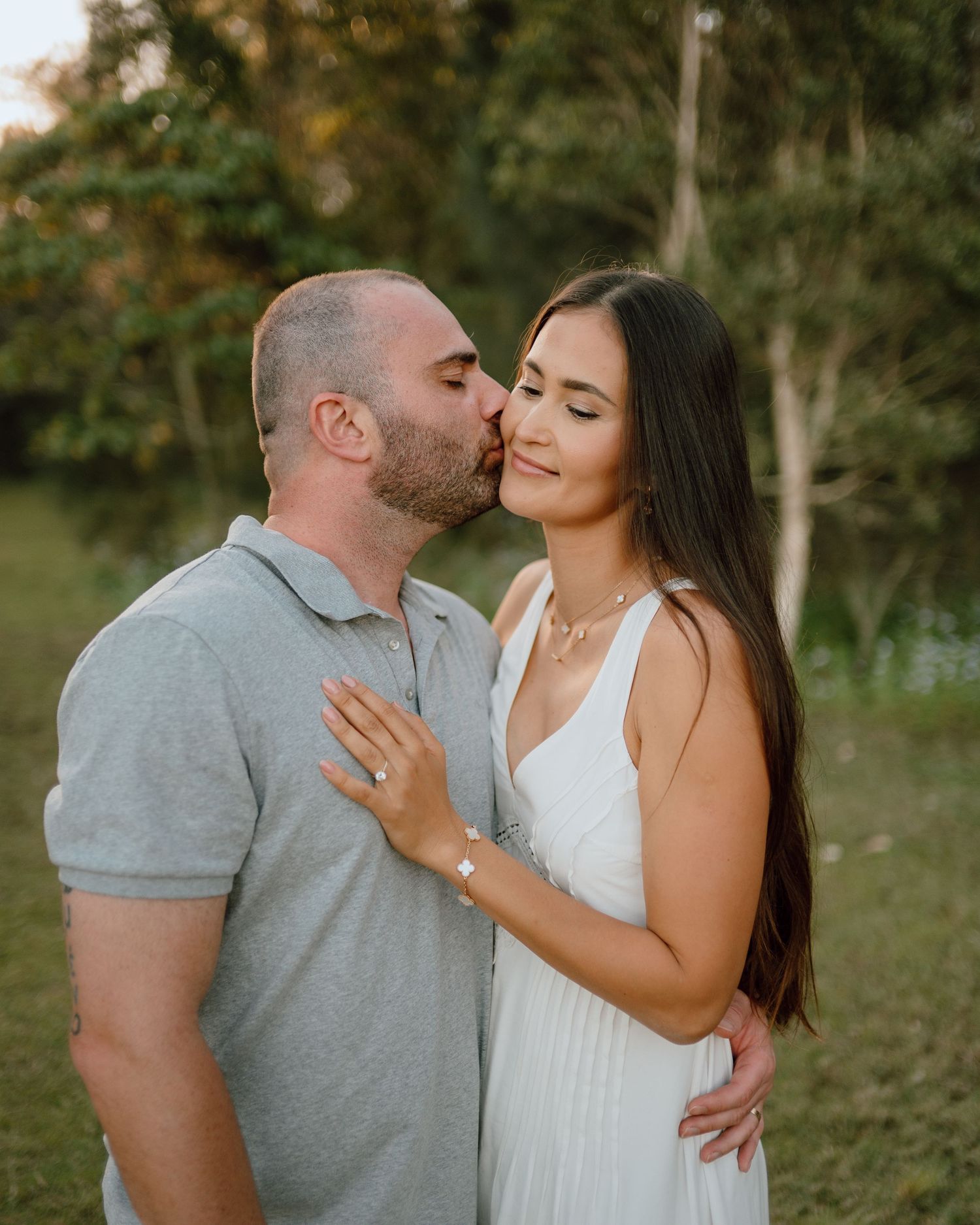 Romantic couple sharing tender moments outdoors in casual attire during a sunset photoshoot.
