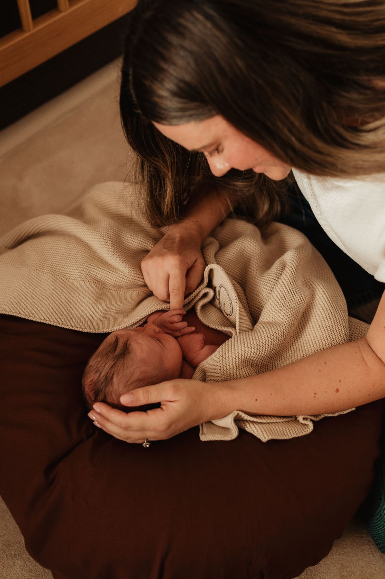 A mother tenderly cradles her newborn baby wrapped in a soft beige knit blanket, gazing down lovingly.