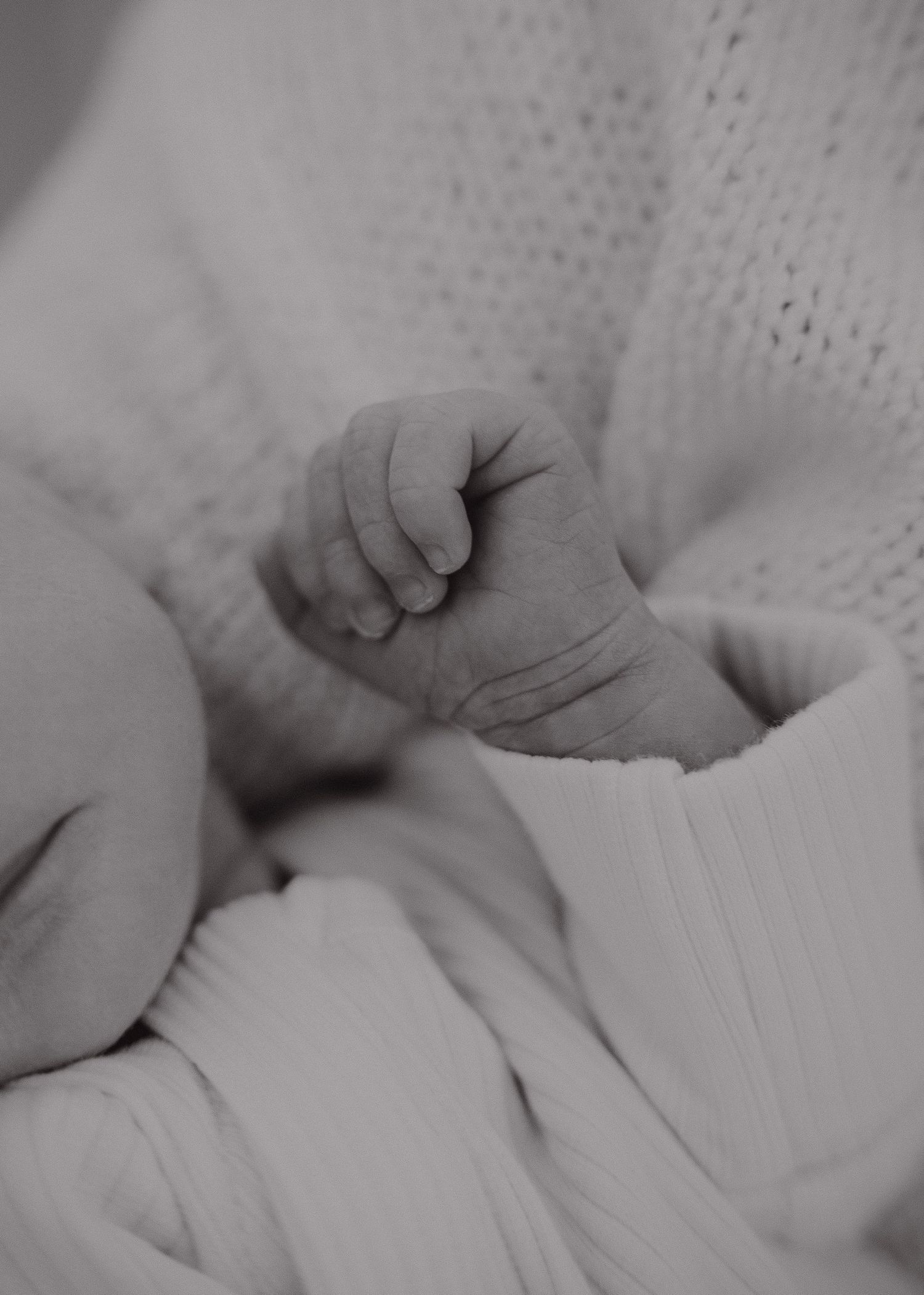 Close-up black and white photo of a tiny newborn baby's hand grasping tightly against soft fabric.