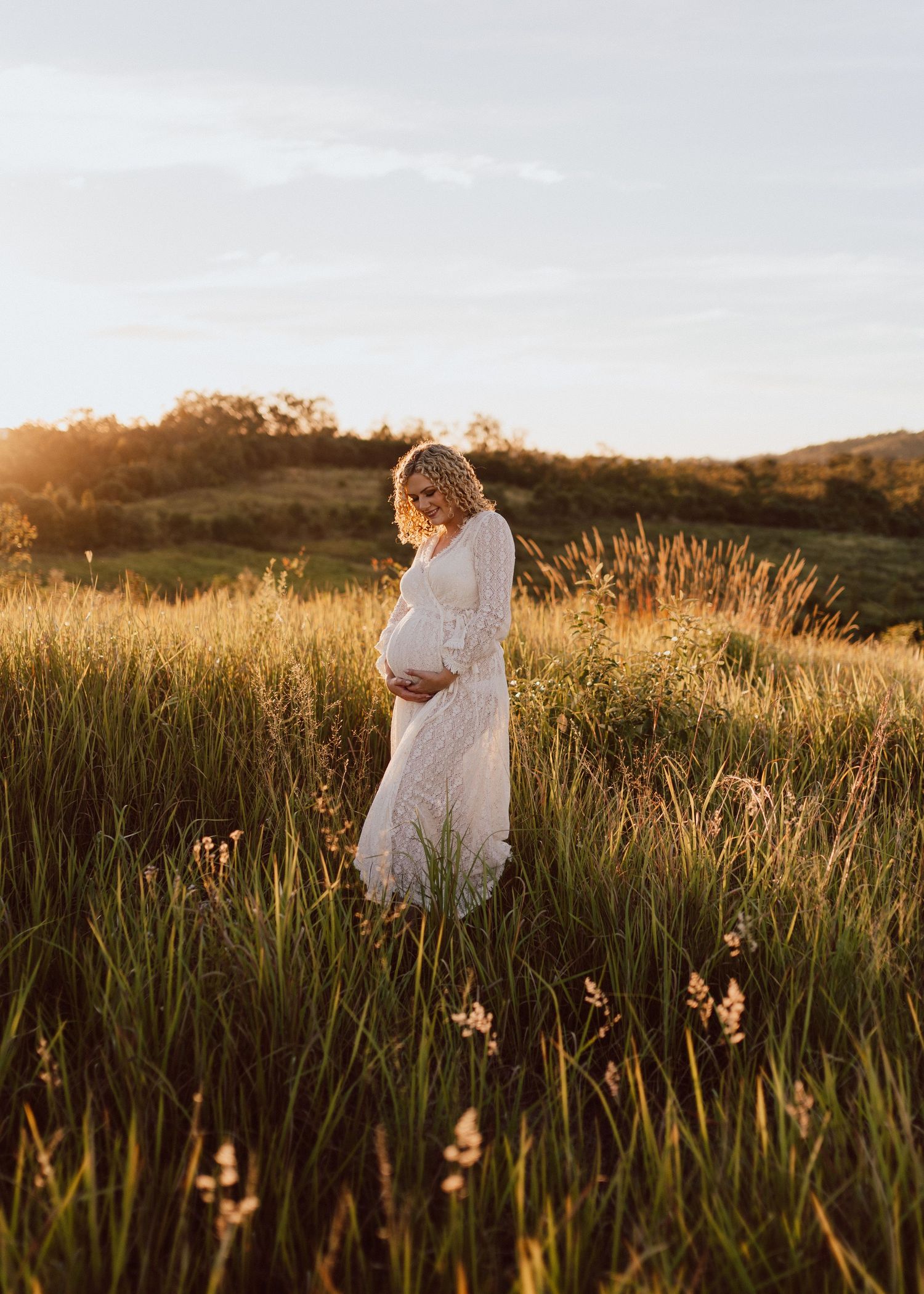 A person in a white dress walks through a golden field of tall grass at sunset creating a dreamy silhouette.