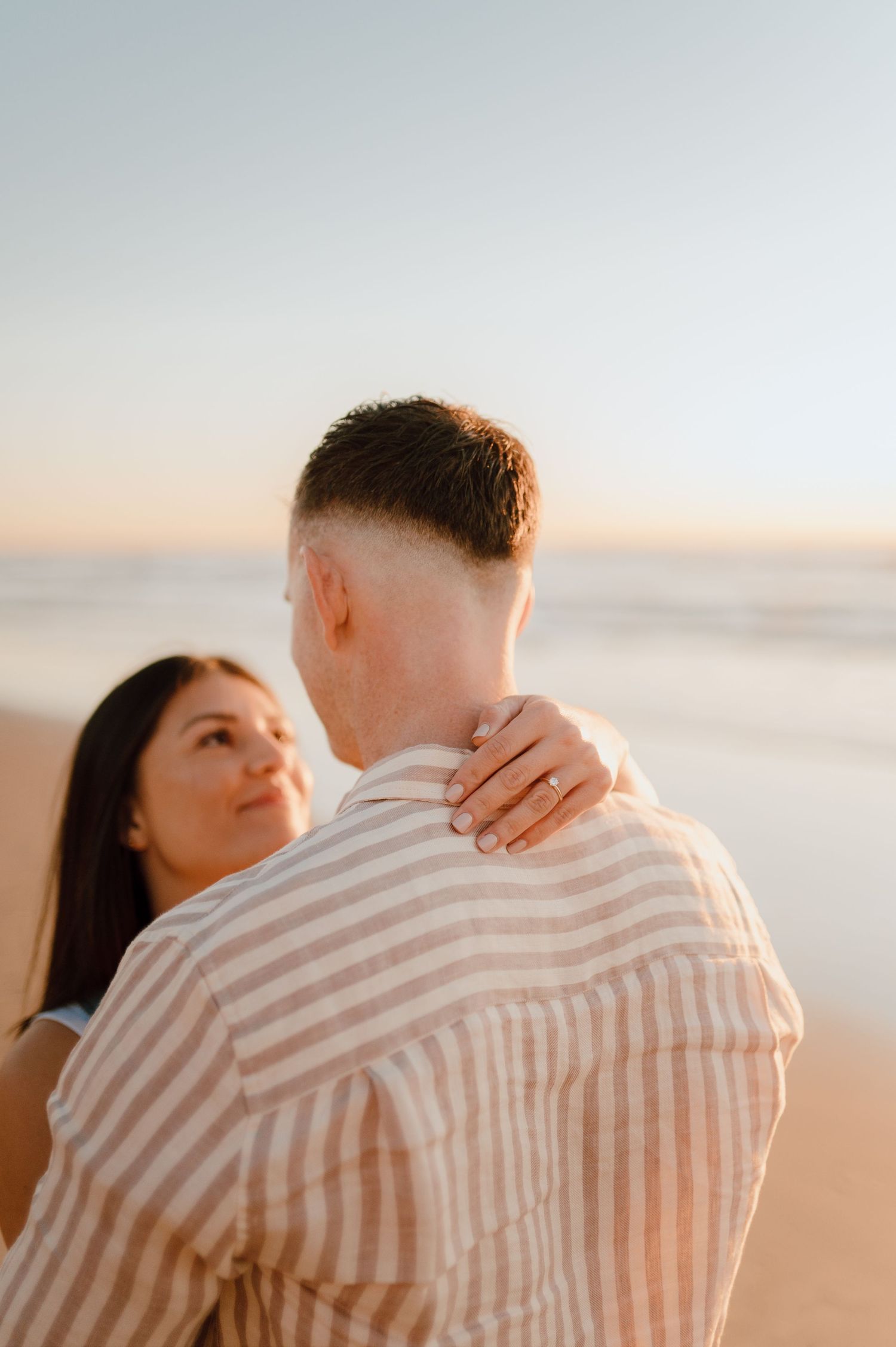 A couple embraces on the beach during golden hour with soft lighting.