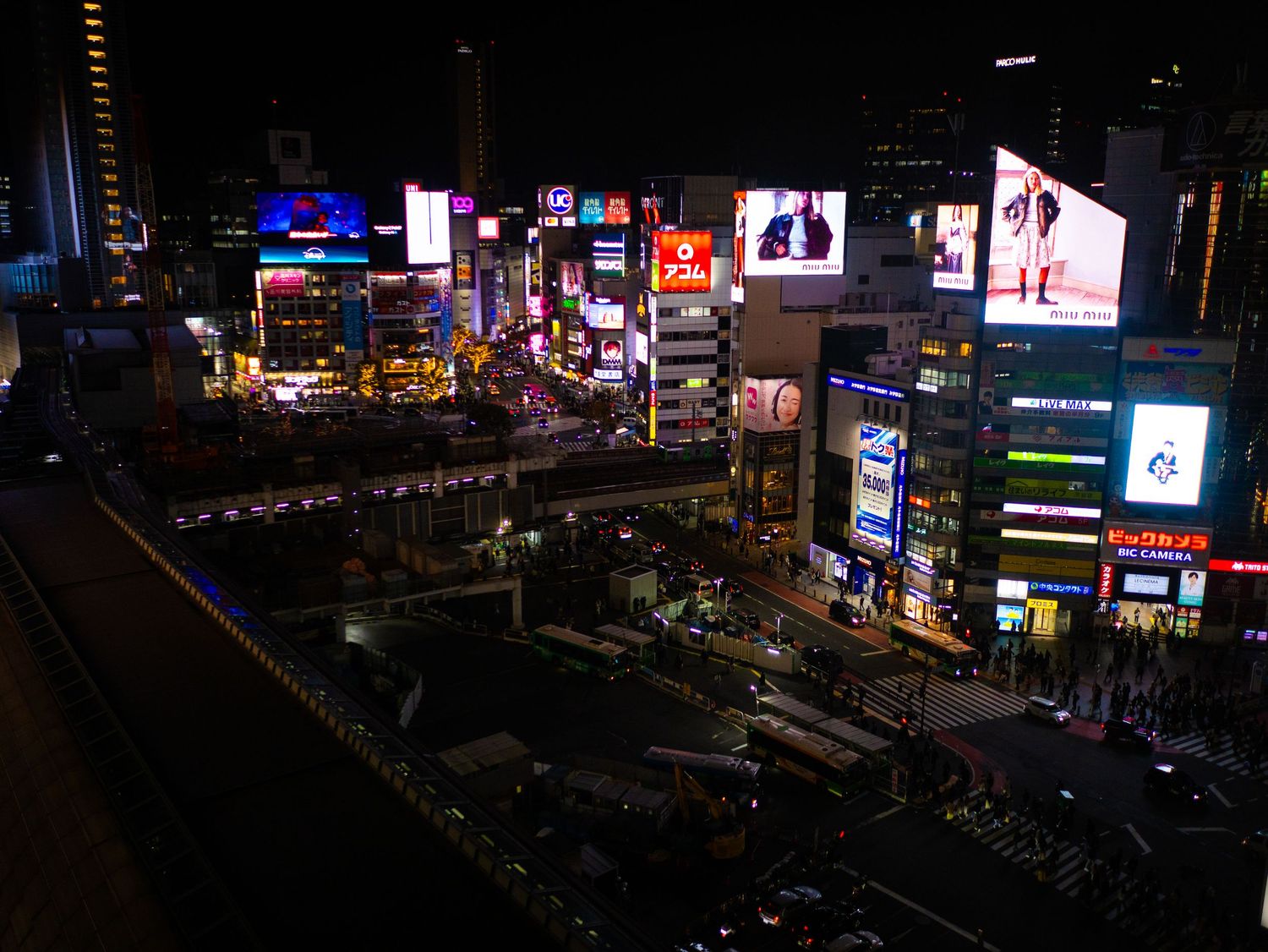 Panoramic nighttime cityscape showing illuminated billboards and buildings in Japan.