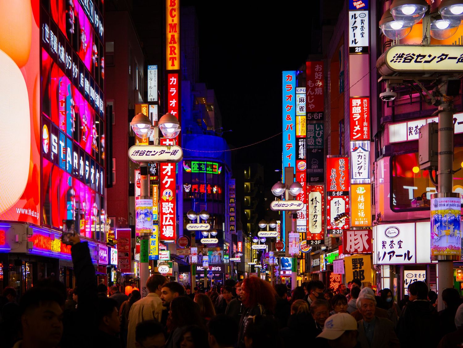 Vibrant neon signs and billboards illuminate a busy nighttime street in Japan's entertainment district.