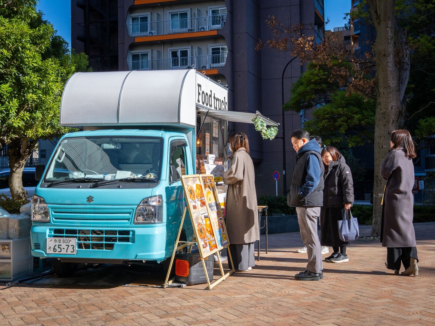 A vintage turquoise van parked outside a building with people gathering nearby.