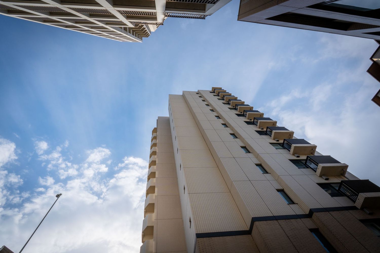 Looking up at a tall modern apartment building with white exterior and balconies against a bright blue sky.
