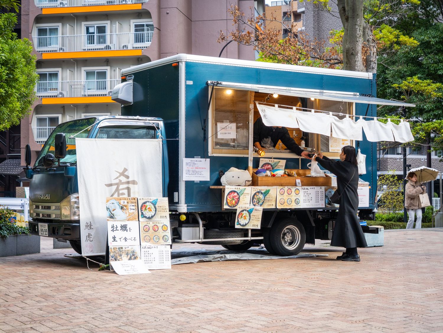 Food trucks parked in a row at an outdoor event with orange and white awnings on a sunny day.
