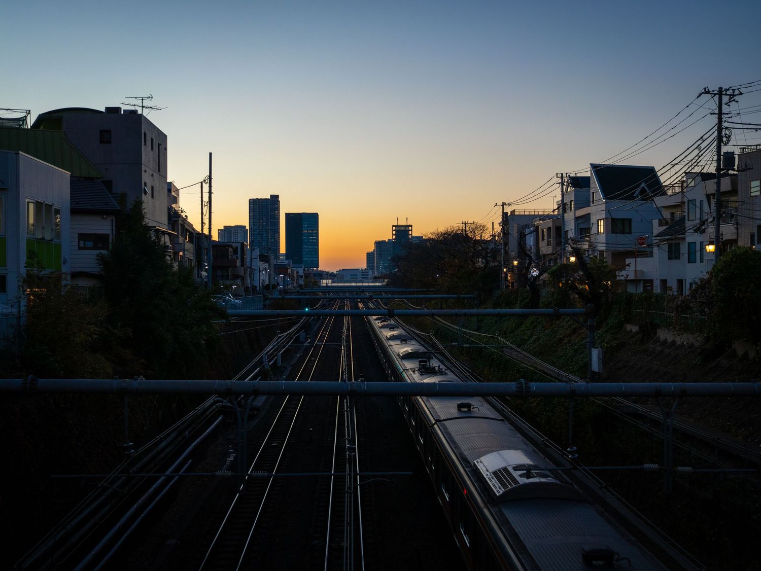 Railroad tracks extend into the distance against a dusky sky with urban buildings silhouetted along the sides.
