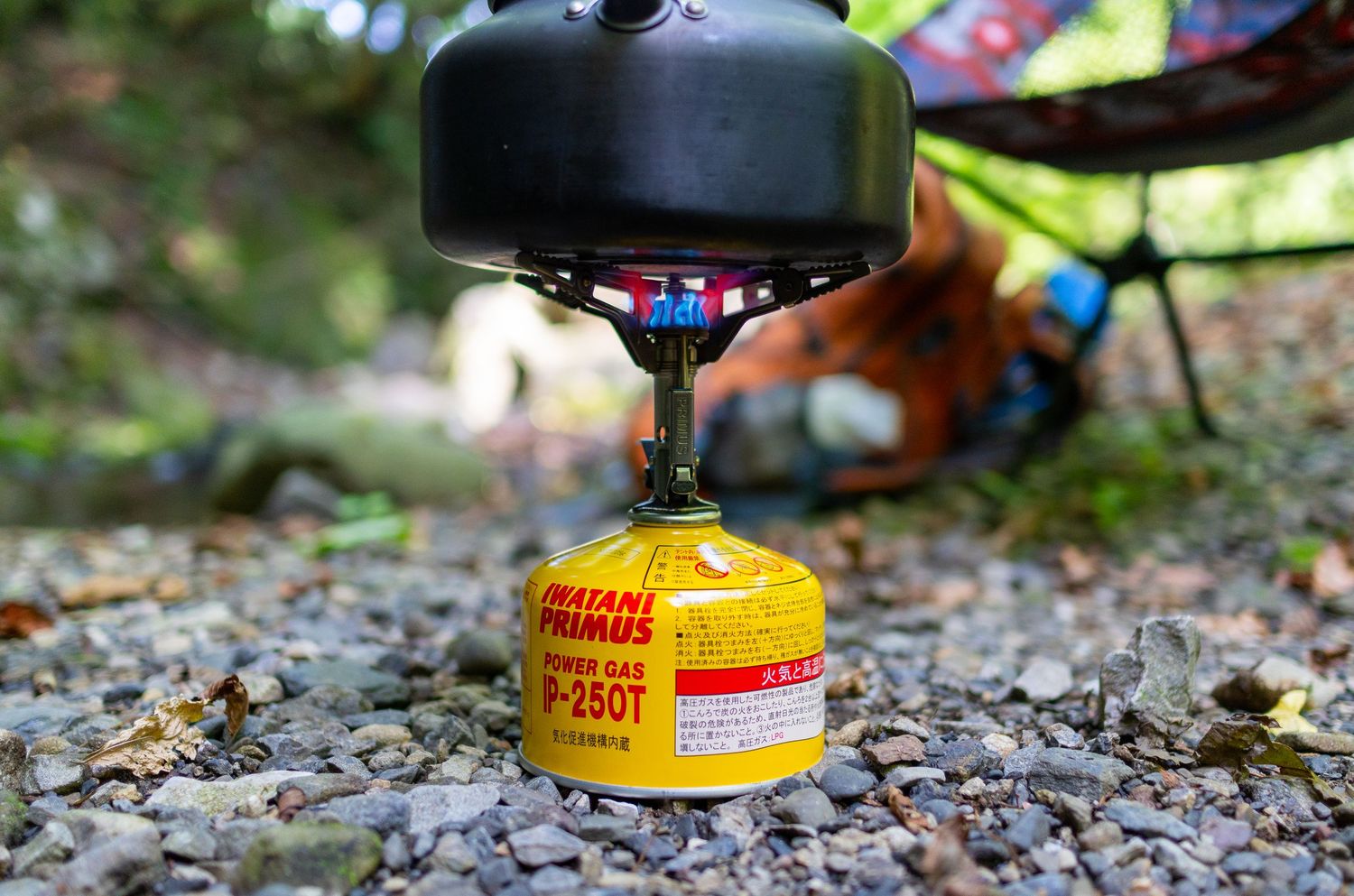 Portable camping stove with yellow fuel canister set up on gravel.