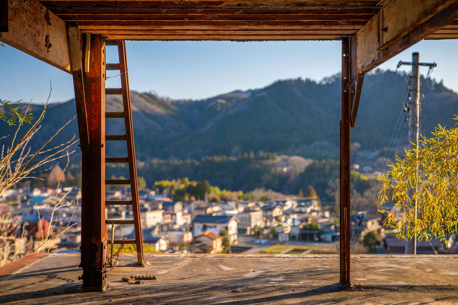 Panoramic mountain view through rustic wooden beams at sunset with distant buildings and trees in autumn colors.