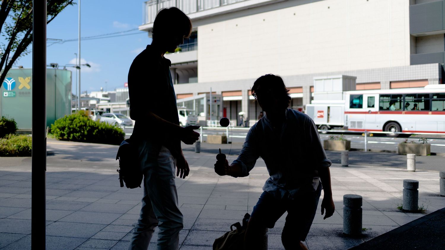 Silhouetted figures walking along an urban sidewalk on a sunny day.