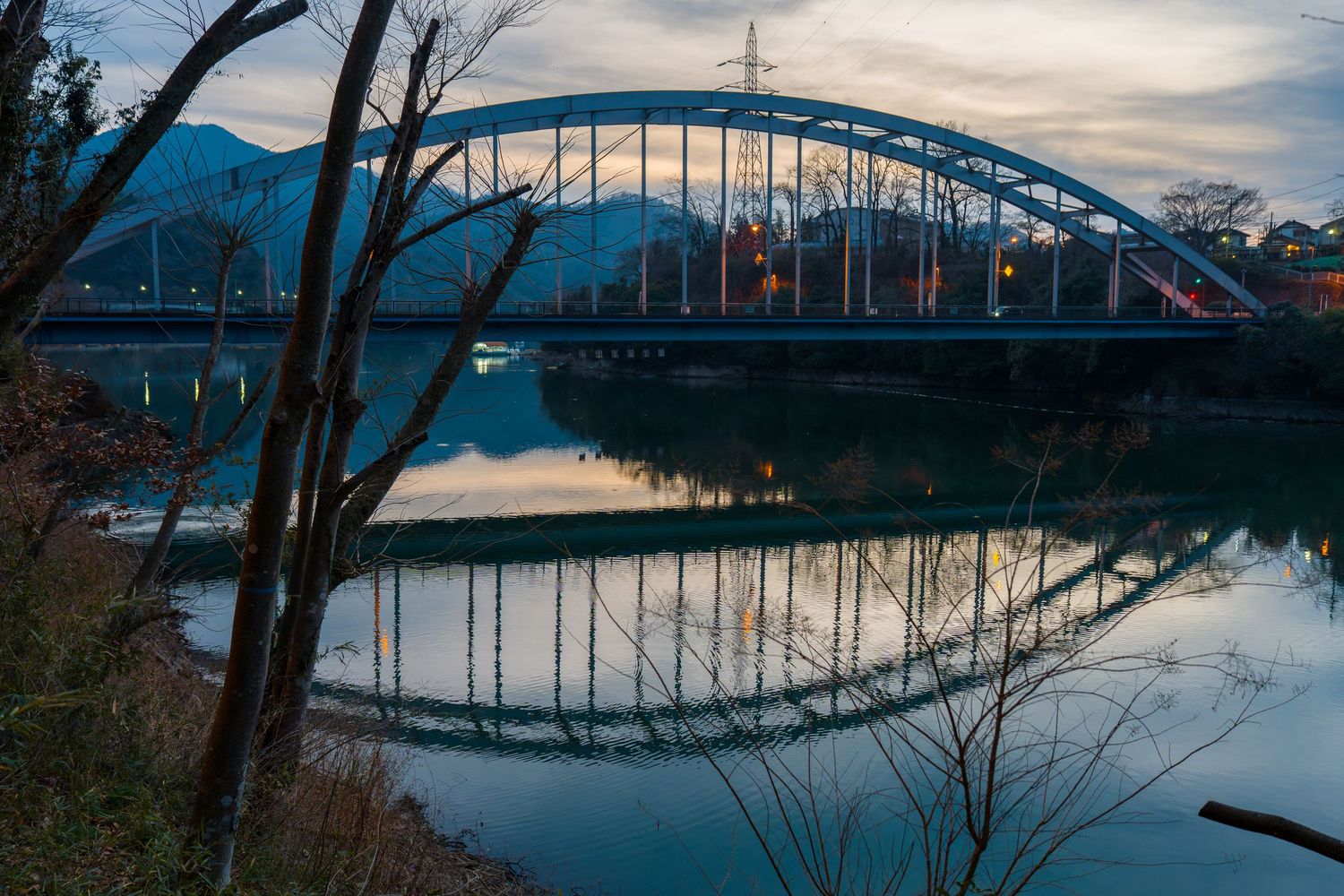 Scenic panoramic view of a curved bridge over calm water reflecting the cloudy sky at dusk.