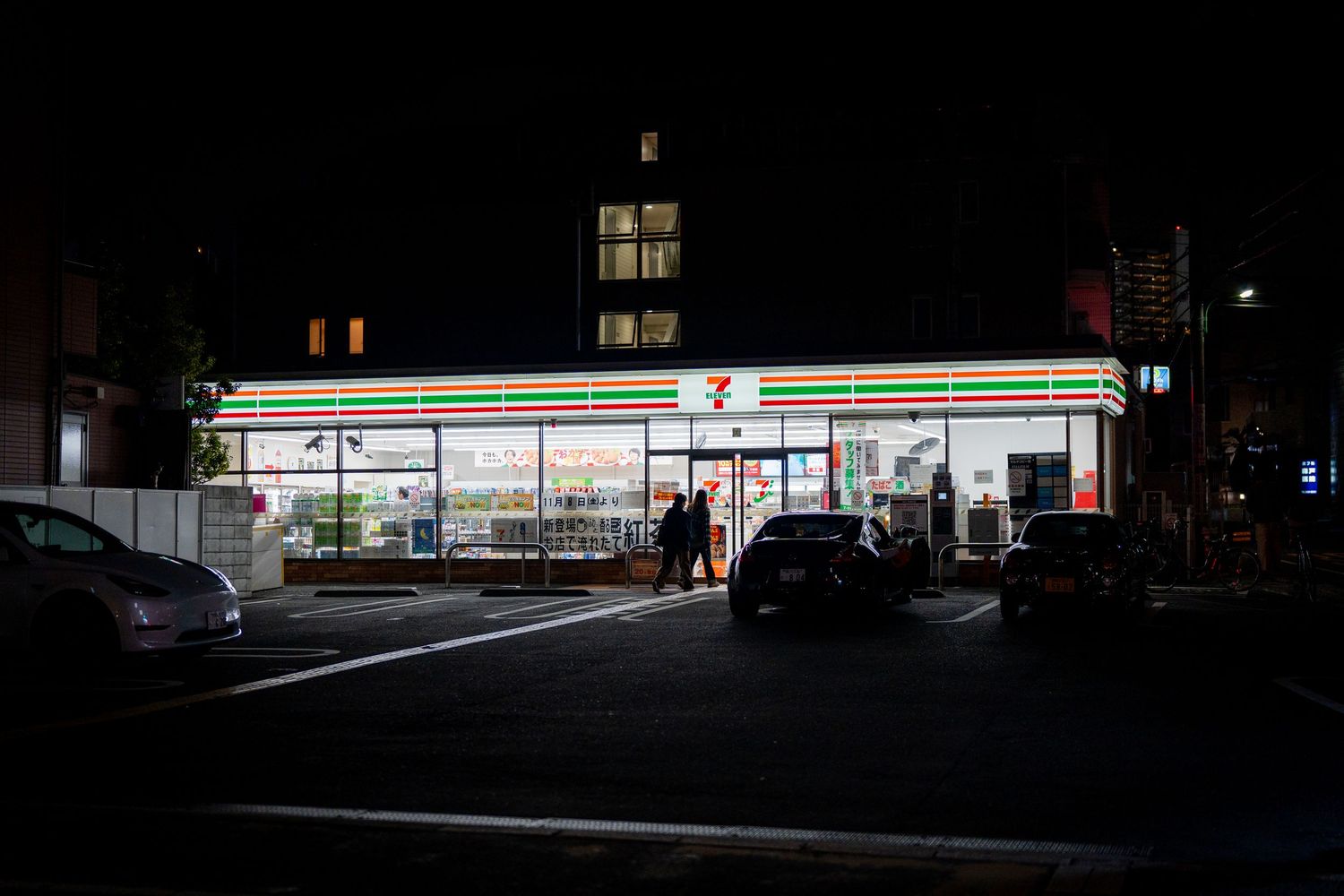 Dimly lit urban street scene with convenience store glowing in the distance at night.
