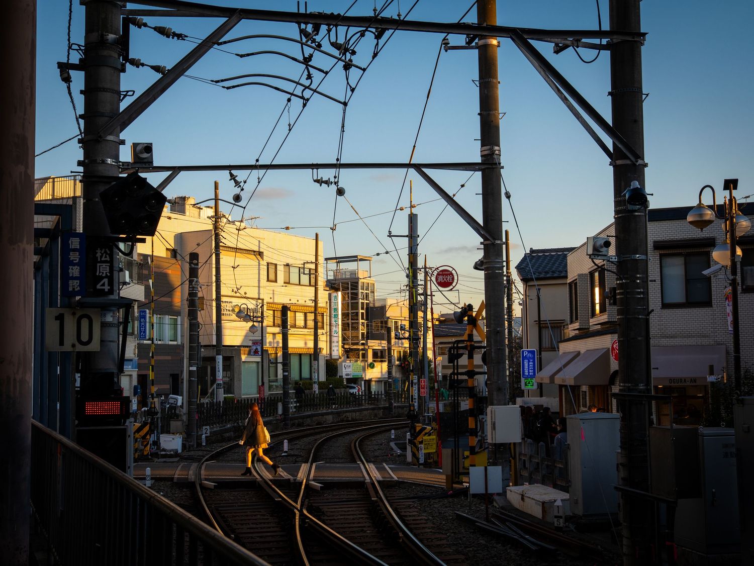 A panoramic view of a Japanese residential street at sunset with power lines and buildings silhouetted against a blue sky.