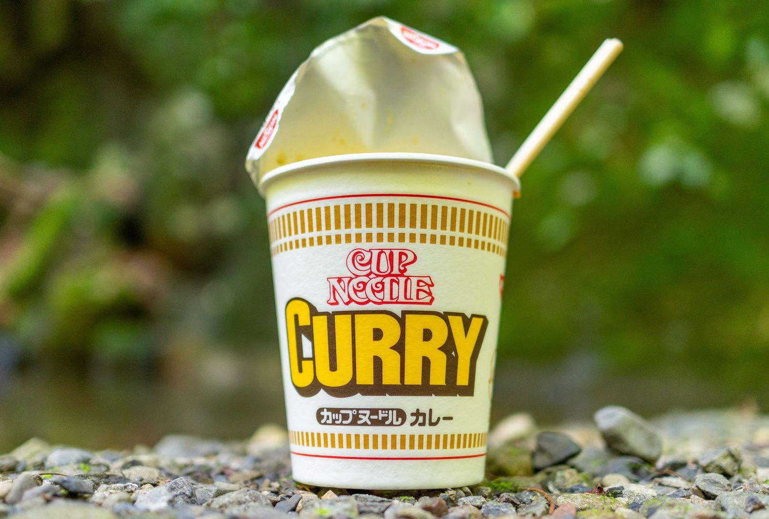Cup Noodle curry instant ramen container placed on rocky ground outdoors.