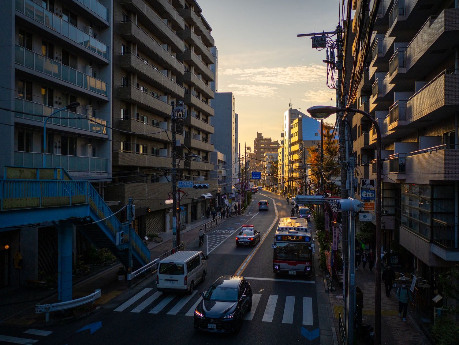 Urban street scene at sunset with apartment buildings casting long shadows and warm golden light.