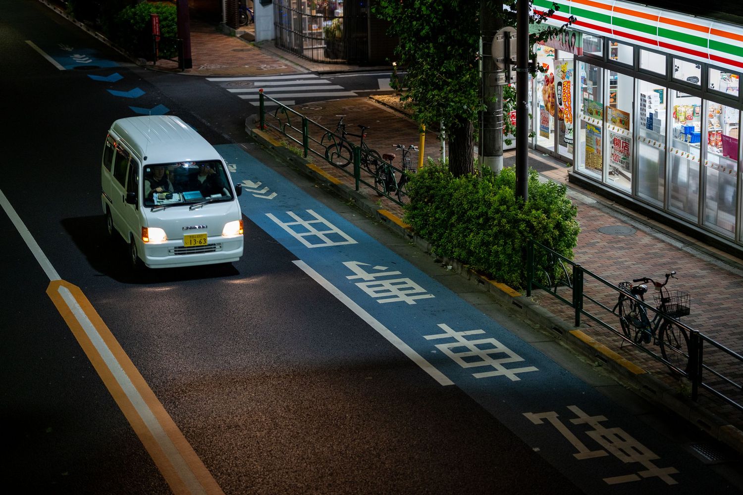 Cars and bicycles parked along a quiet residential street with convenience store signage.