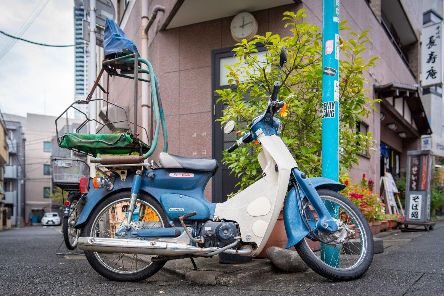 Parked bicycles and scooters line up against a building wall in an urban Japanese setting.