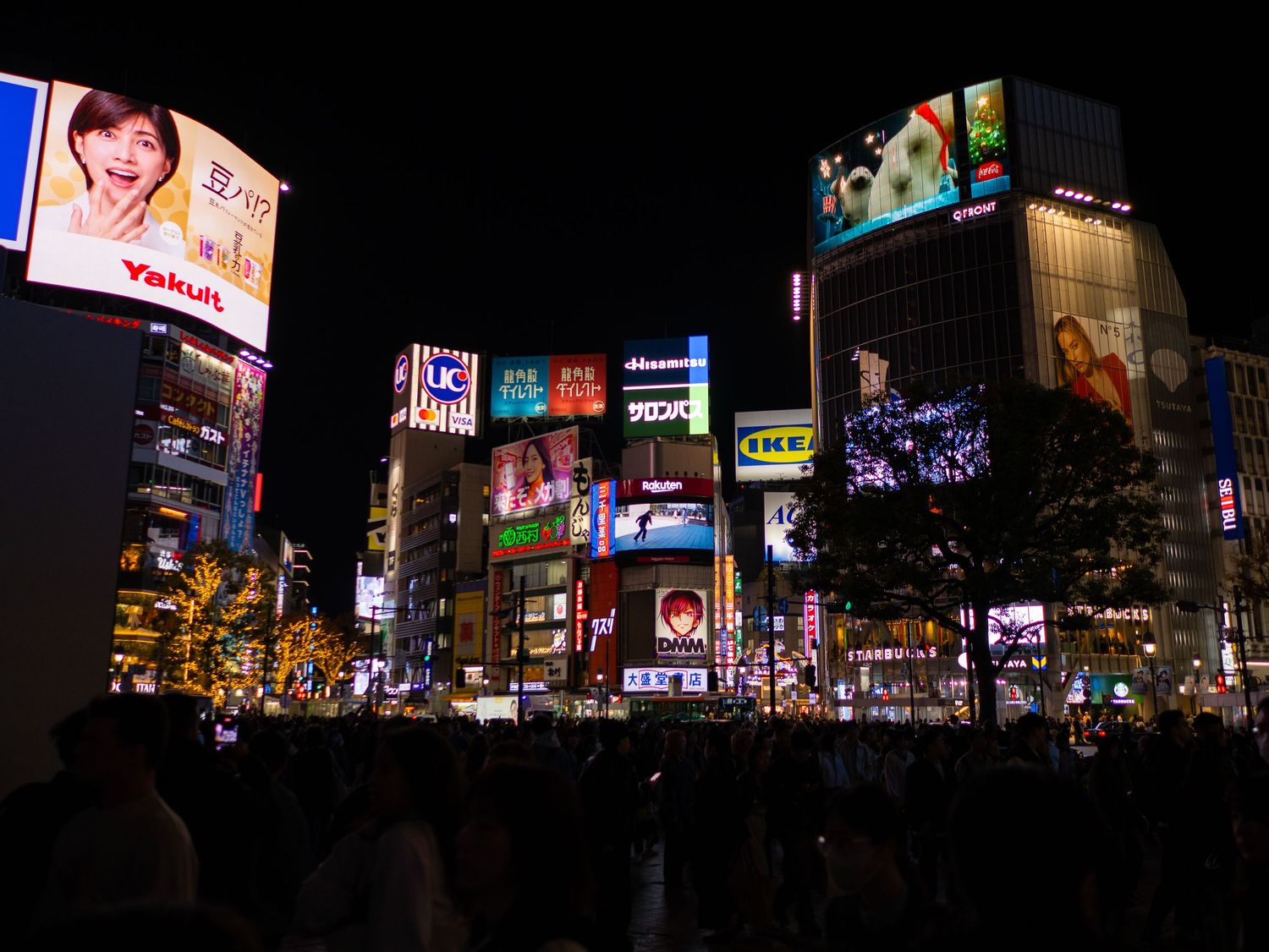 Wide view of bright electronic billboards and advertisements lighting up a Japanese city street at night.