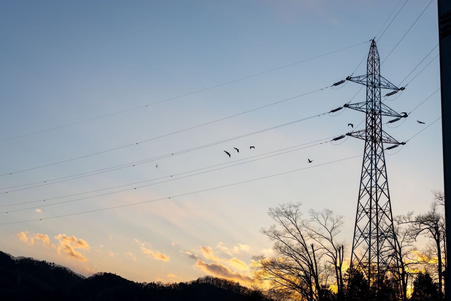 High voltage power transmission lines and towers silhouetted against a colorful sunset sky with clouds.