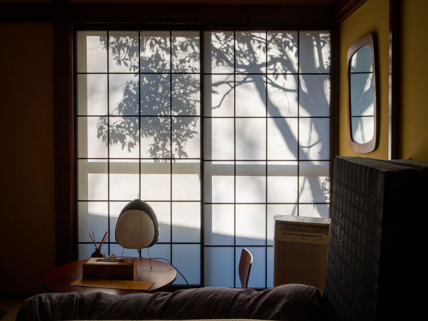 A row of large windows in an old building interior lets in natural light while showcasing tree branches outside.