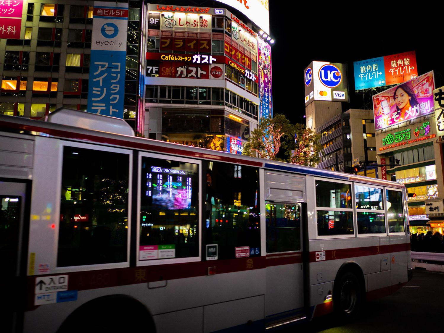 Urban street scene with buses and bright neon signage in Tokyo's entertainment district.