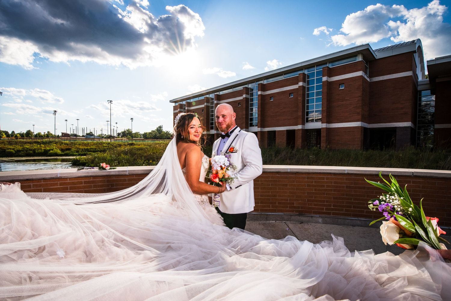 Wedding photos on a bright sunny day with dramatic clouds and flowing bridal veil in the wind.