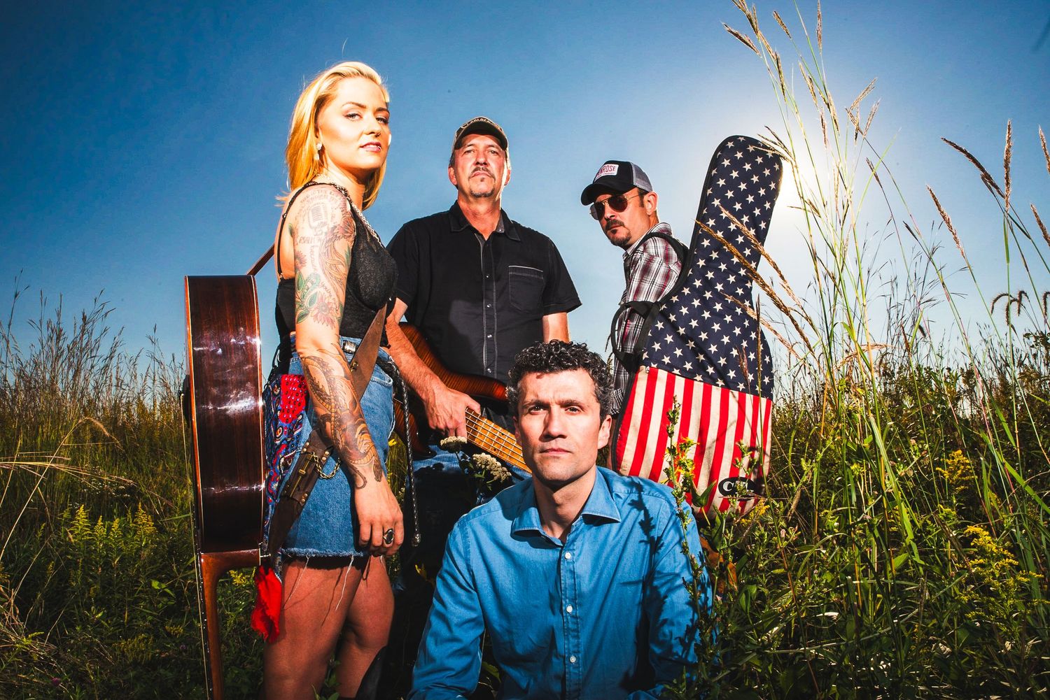 A group poses outdoors in a grassy field at sunset with an American flag and vintage suitcase as props.