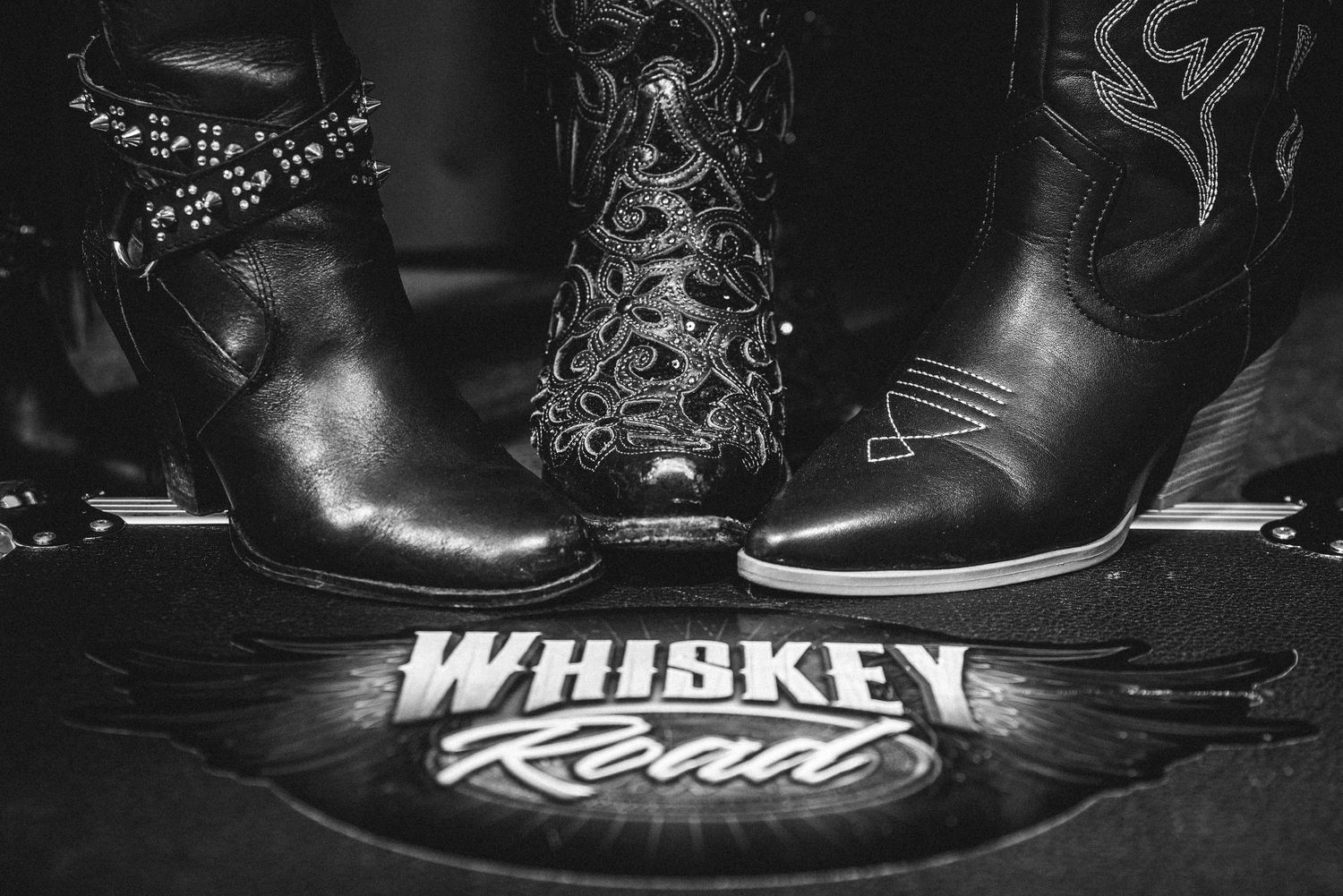 Three pairs of leather cowboy boots stand on a Whiskey River branded surface.