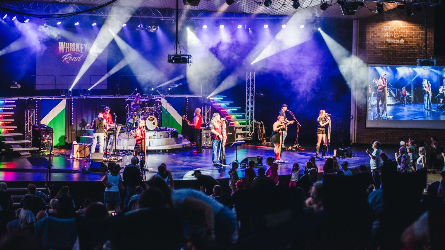 A wide shot of a concert stage with blue lighting and multiple performers entertaining a crowd.