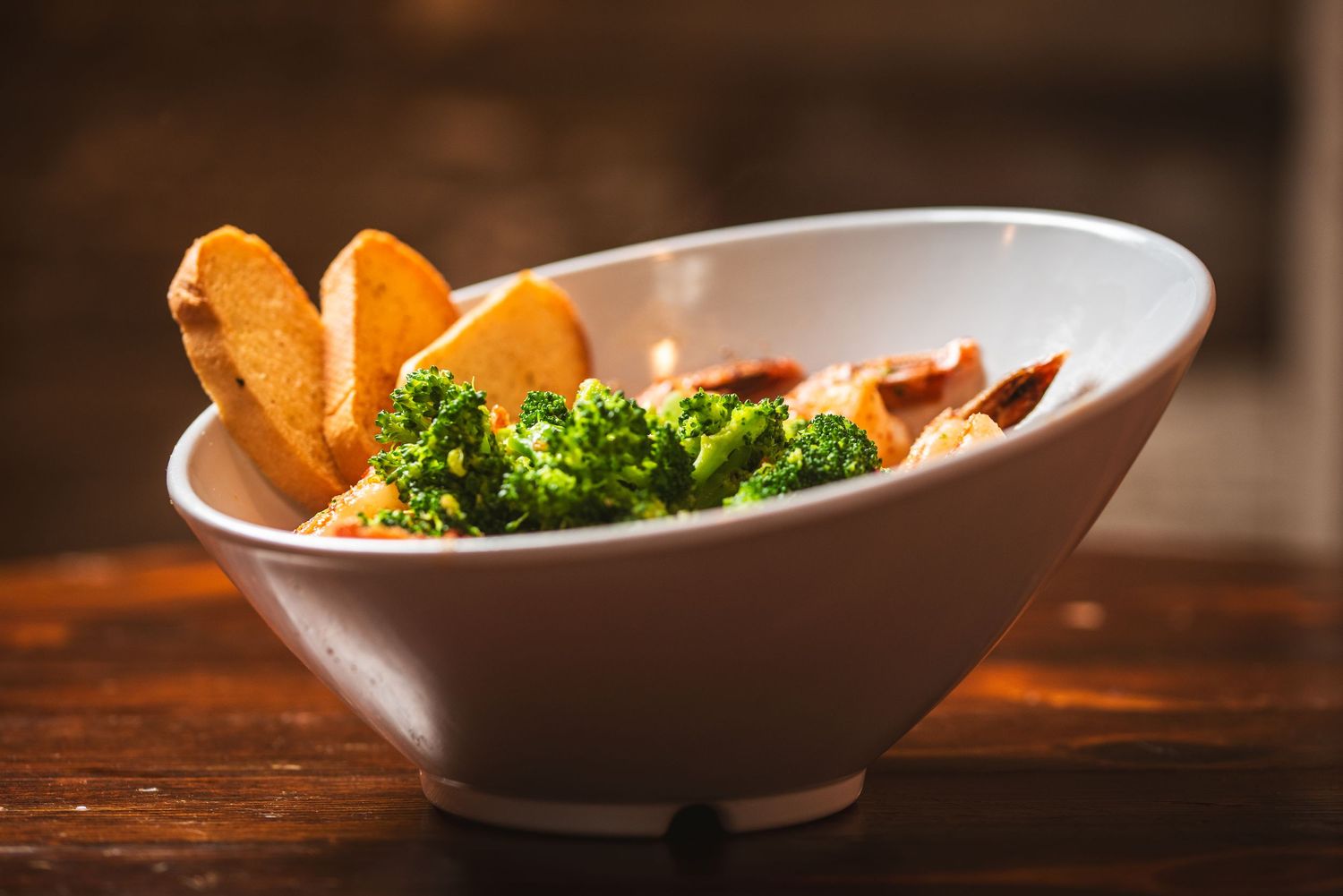 A close-up view of roasted sweet potatoes and broccoli in a white ceramic bowl on a rustic wooden table.