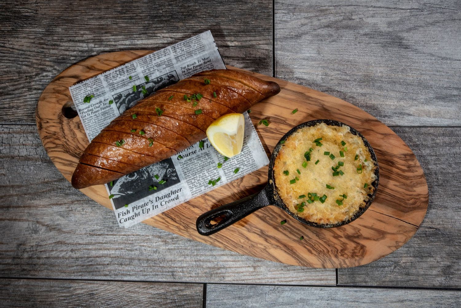 Olive wood cutting board with bread and herb butter arranged in a rustic setting on a gray wooden surface.