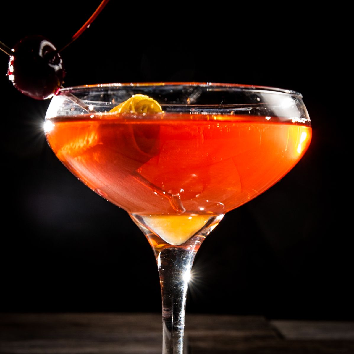 Orange cocktail in martini glass against dark background.
