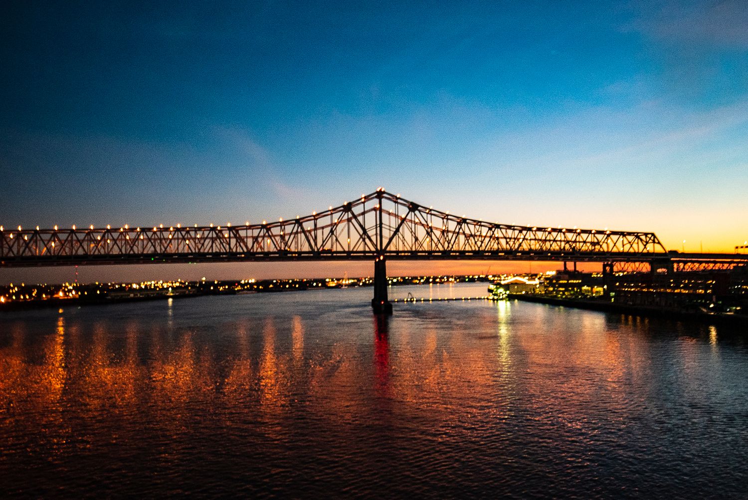 Bridge silhouetted against vibrant sunset sky with orange reflections on calm river water in New Orleans, LA.