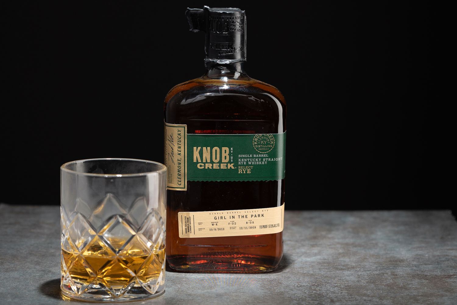Whiskey glass and bottle of Knob Creek bourbon on dark background with moody lighting.