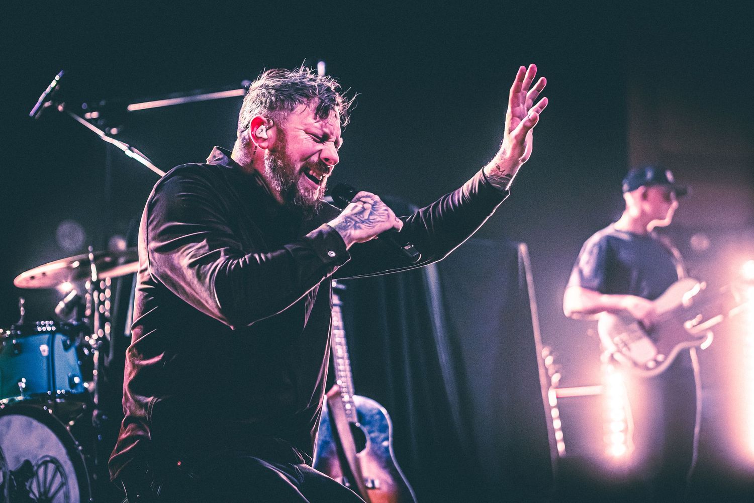 A passionate performer gestures with raised hand while singing into a microphone on stage.