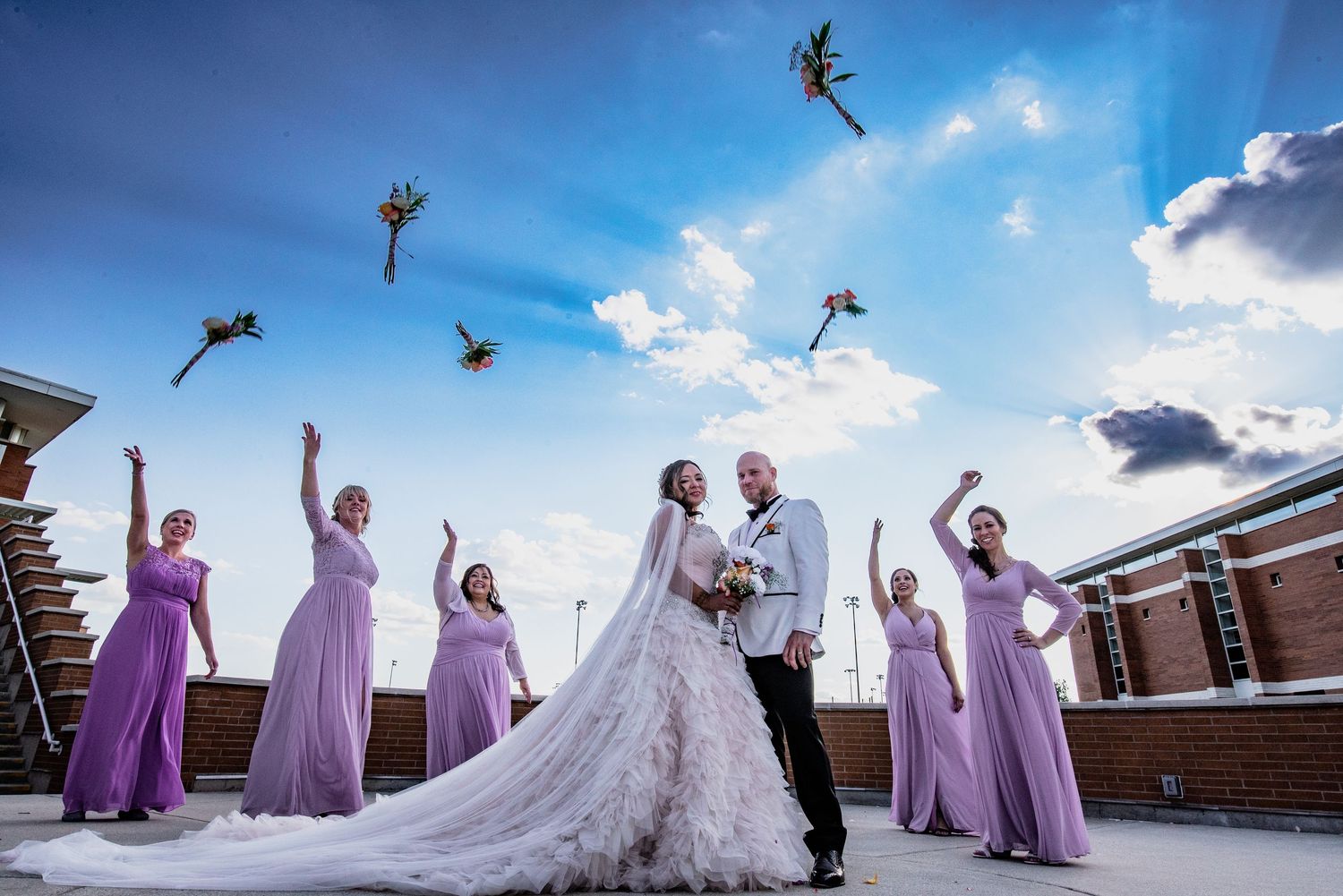 Wedding party in purple dresses celebrates joyfully against a bright blue sky.