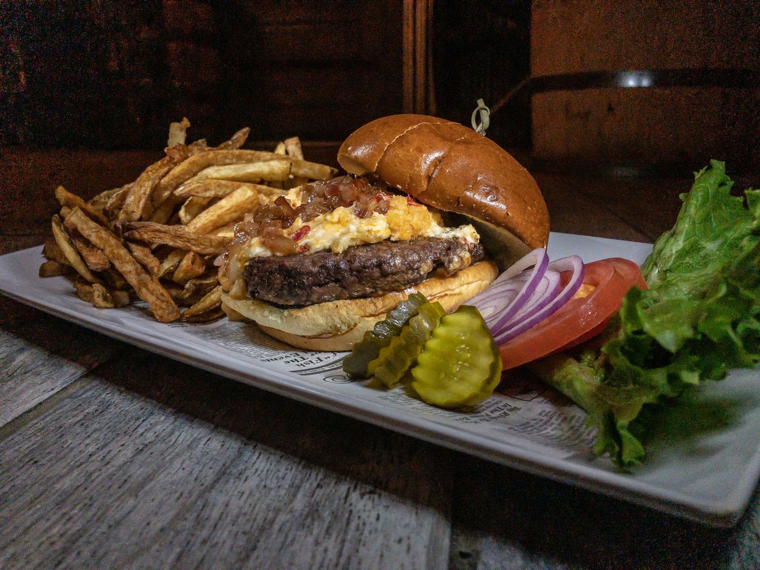 Gourmet burger served with french fries, pickles and fresh vegetables on rectangular plate.