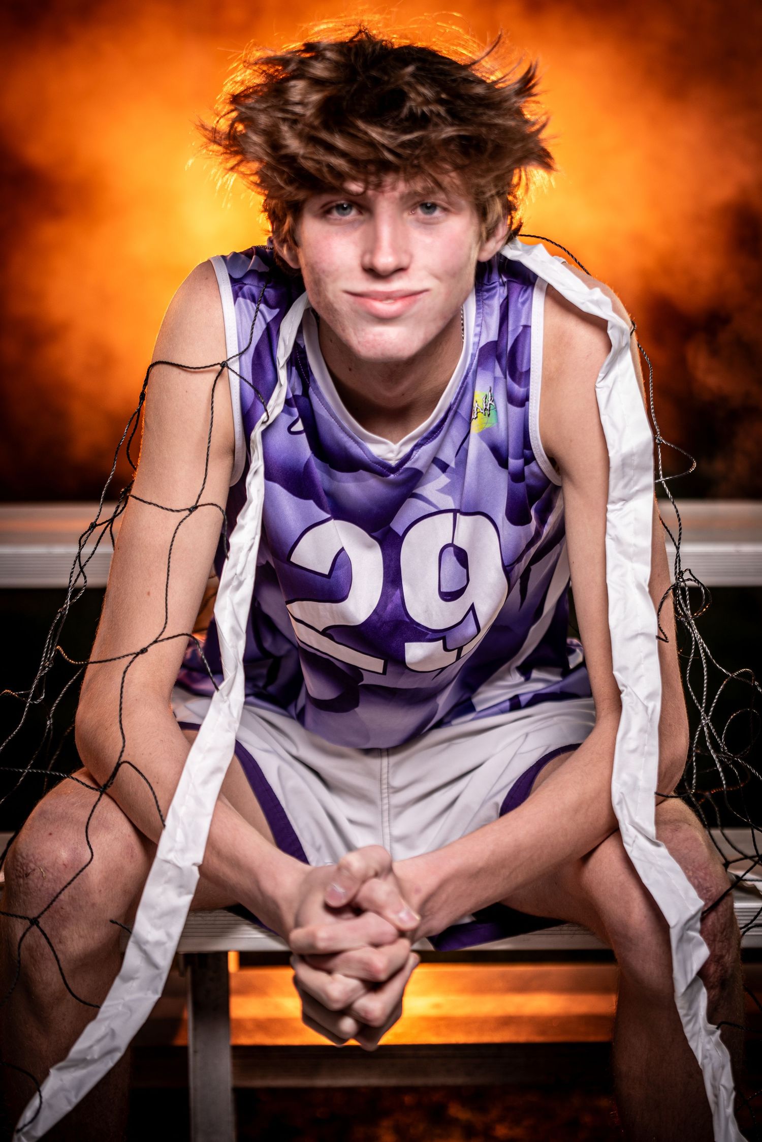 Senior Photos in New Lenox, IL featuring a male volleyball player sitting on a bench with backlit dramatic orange lighting.