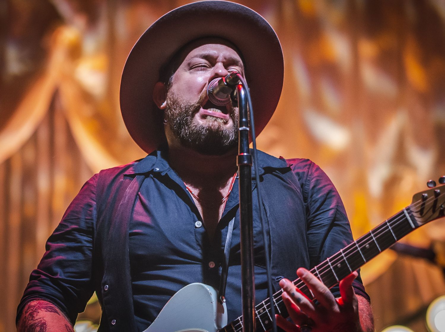 A passionate country music performance with a singer in a brown hat playing guitar against fiery backdrop.