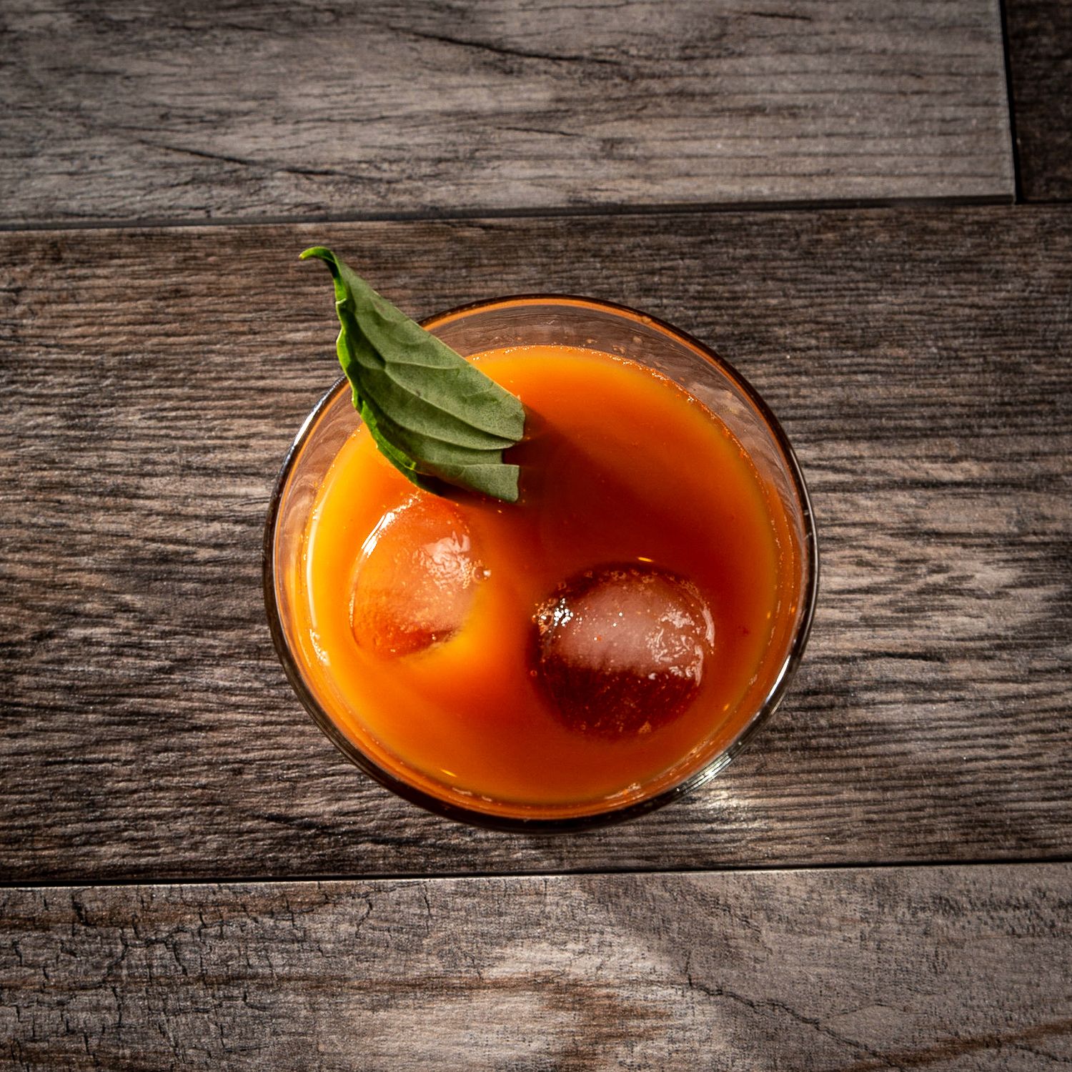 Orange cocktail with garnish served in a martini glass on rustic wooden surface in dramatic lighting.