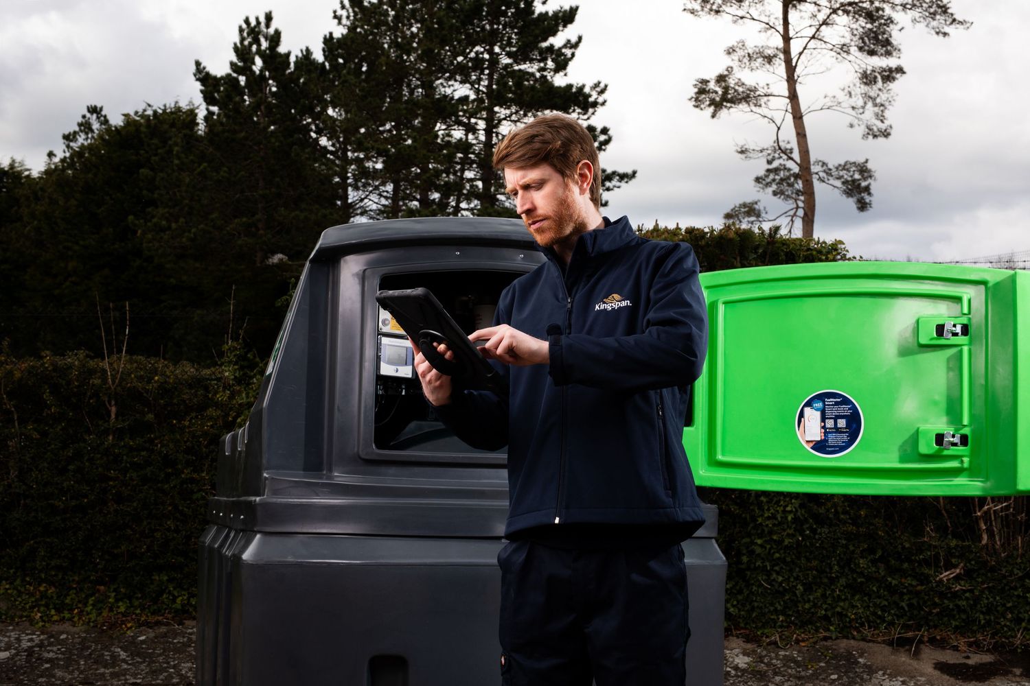 Kingspan engineer using tablet device beside green and grey outdoor fuel storage tank. Kingspan Water & Energy