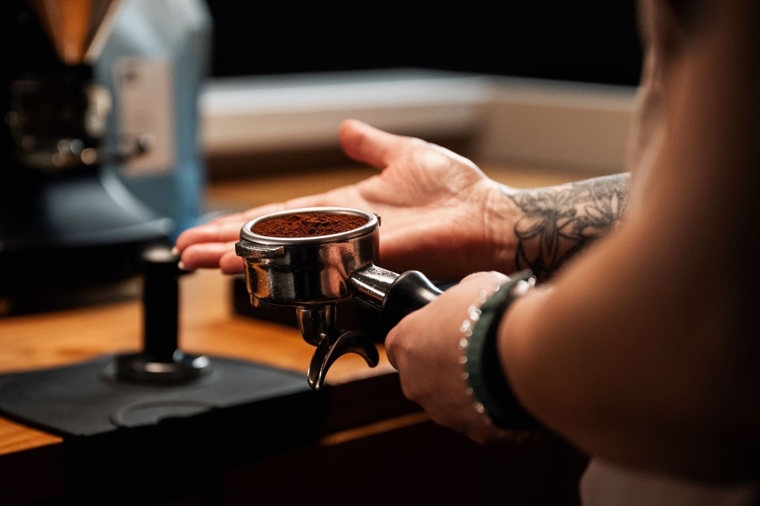 Tattooed barista holding a coffee portafilter filled with ground espresso coffee. Bailies Coffee Roasters
