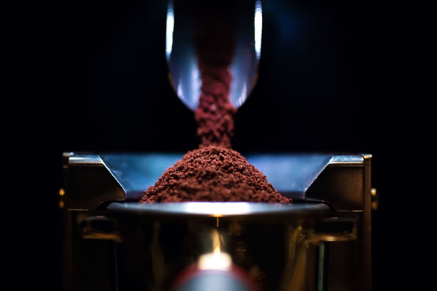 Close-up of fresh ground coffee being dispensed into a golden portafilter with dramatic lighting. Bailies Coffee Roasters