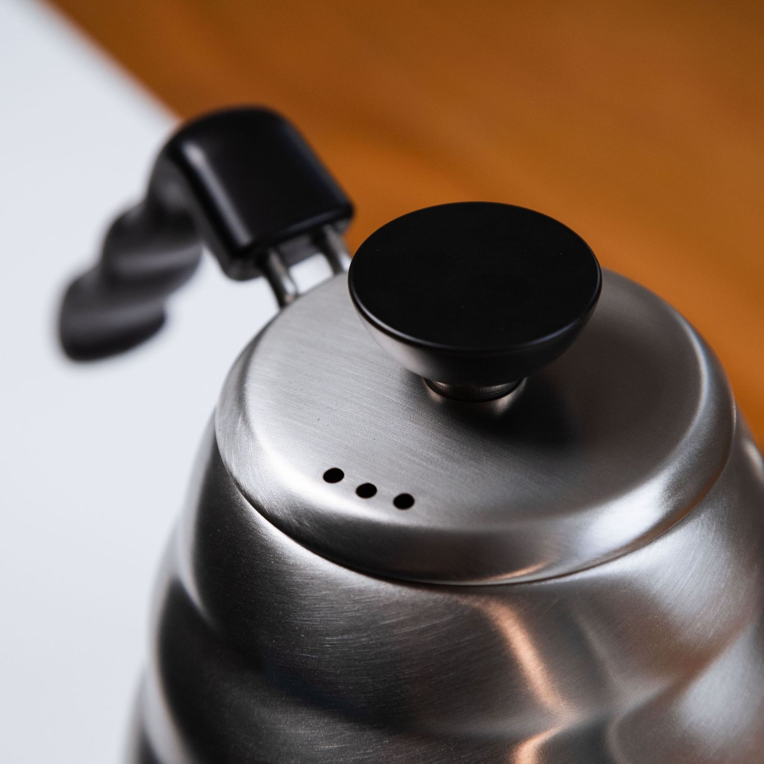 Close-up of a stainless steel gooseneck kettle lid with black knob for pour-over coffee. Bailies Coffee Roasters