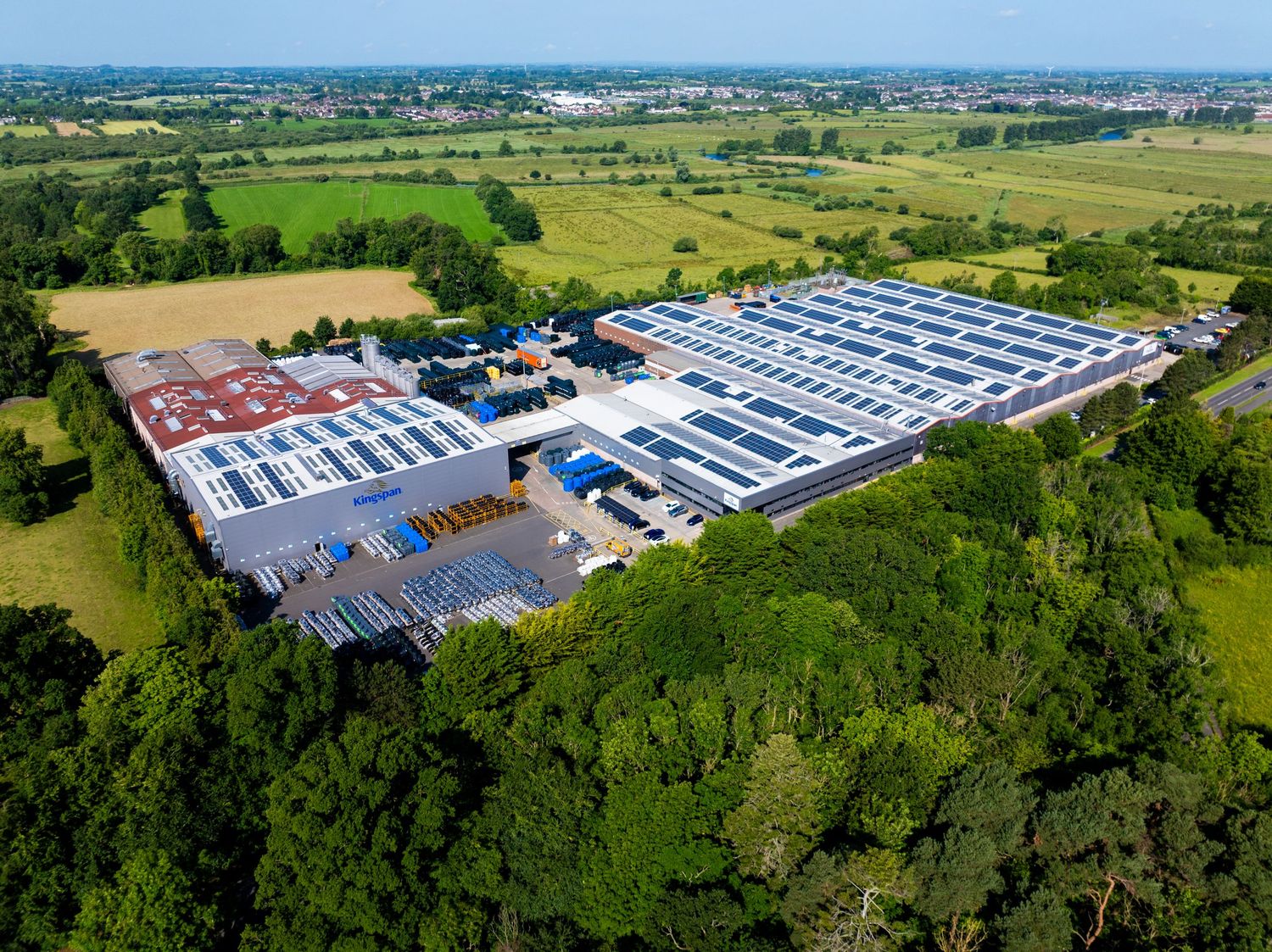 Aerial view of a large industrial facility with solar panels on rooftops surrounded by green fields. Kingspan Water & Energy