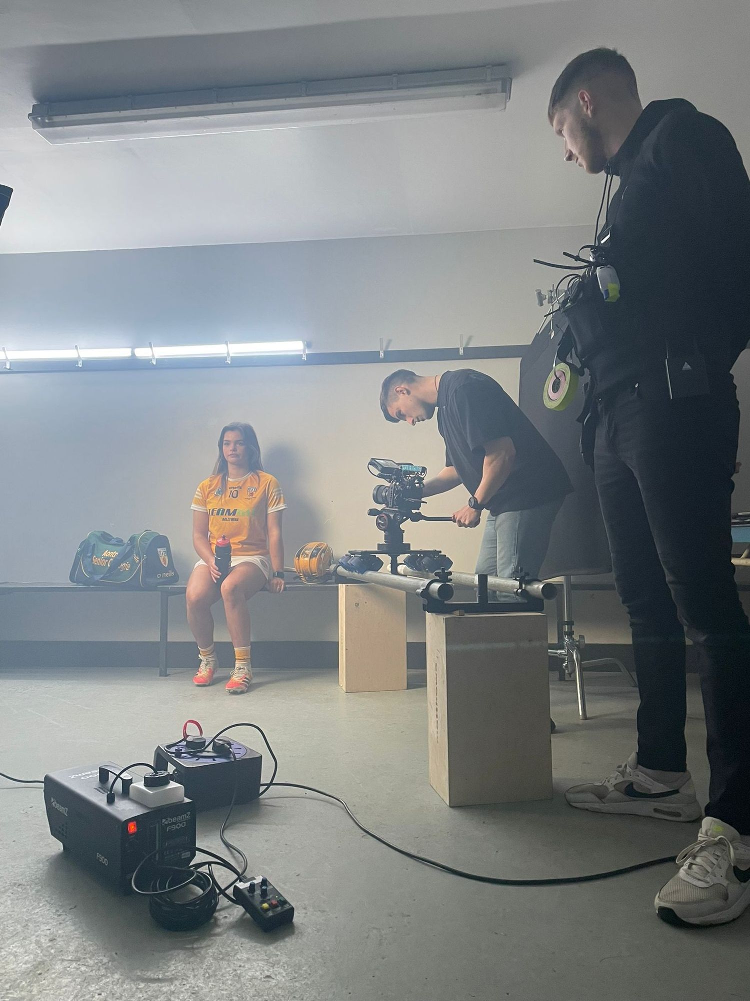 Film crew sets up a professional camera to record a female GAA player in an orange jersey. Ulster GAA